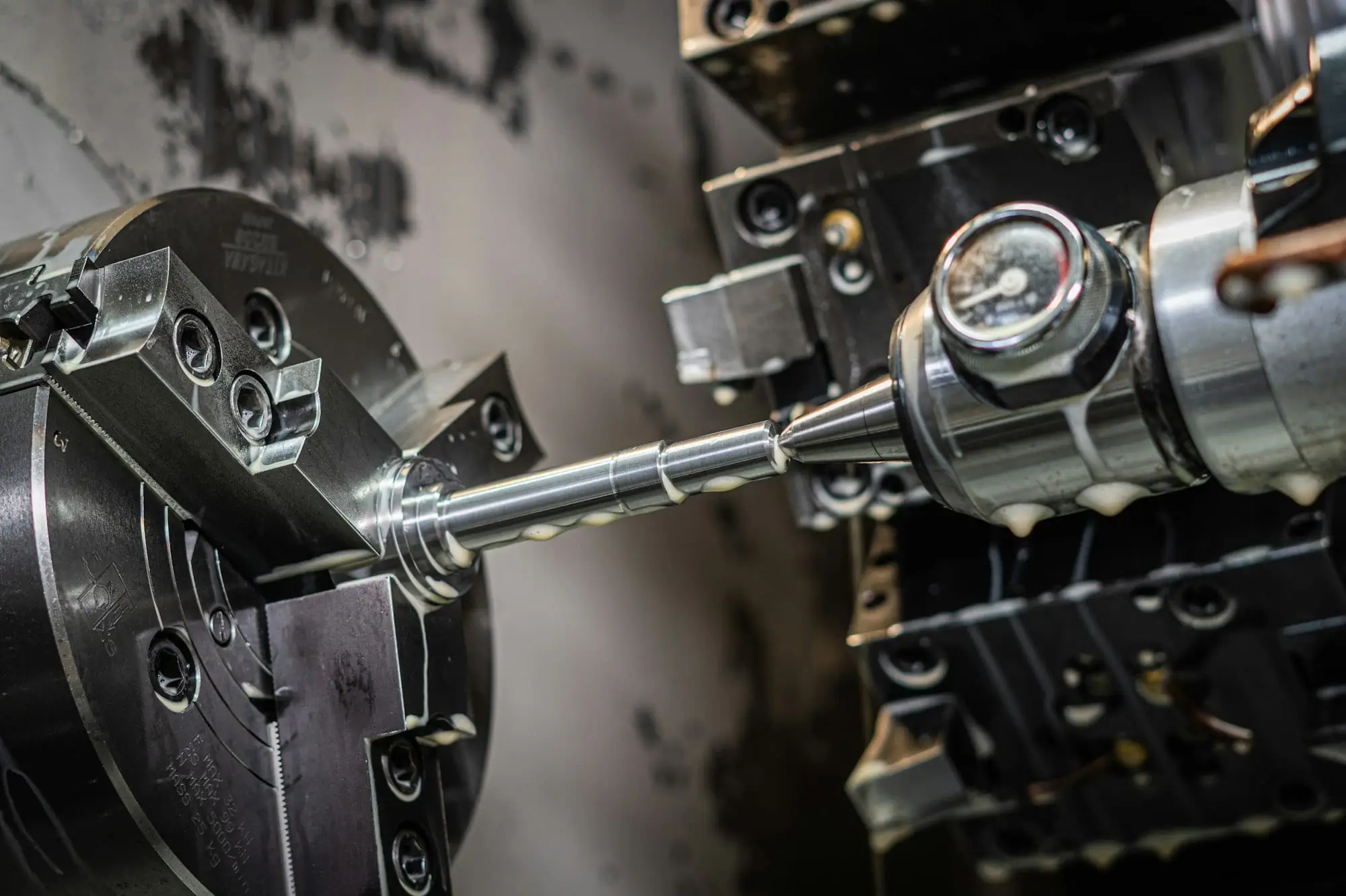 A steel shaft being turned on a CNC lathe, clamped in a three-jaw chuck and supported by a live centre