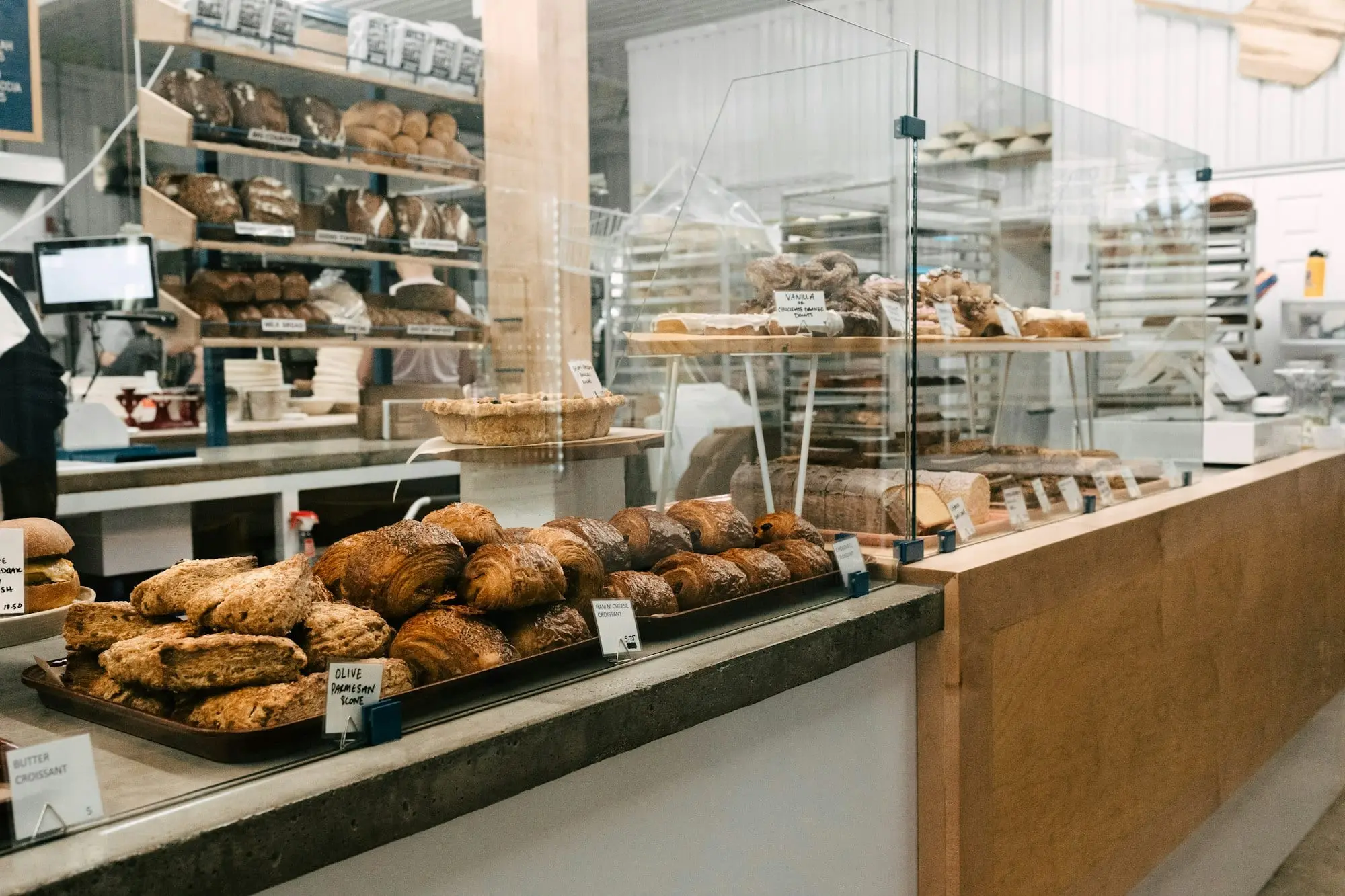 The counter of a small local bakery with trays of pastries and shelves of bread behind the glass